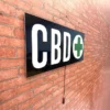 CBD LED sign with a green cross, hanging on a red brick wall
