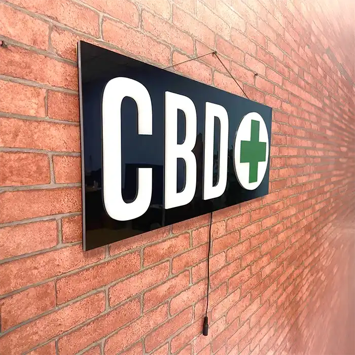 CBD LED sign with a green cross, hanging on a red brick wall