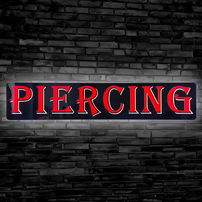 LED Neon Piercing Sign with Red glowing letters on black background hanging on Brick wall.