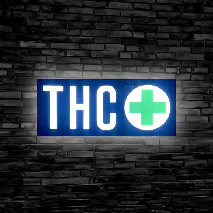 Lit up THC sign with green cross against a black brick wall