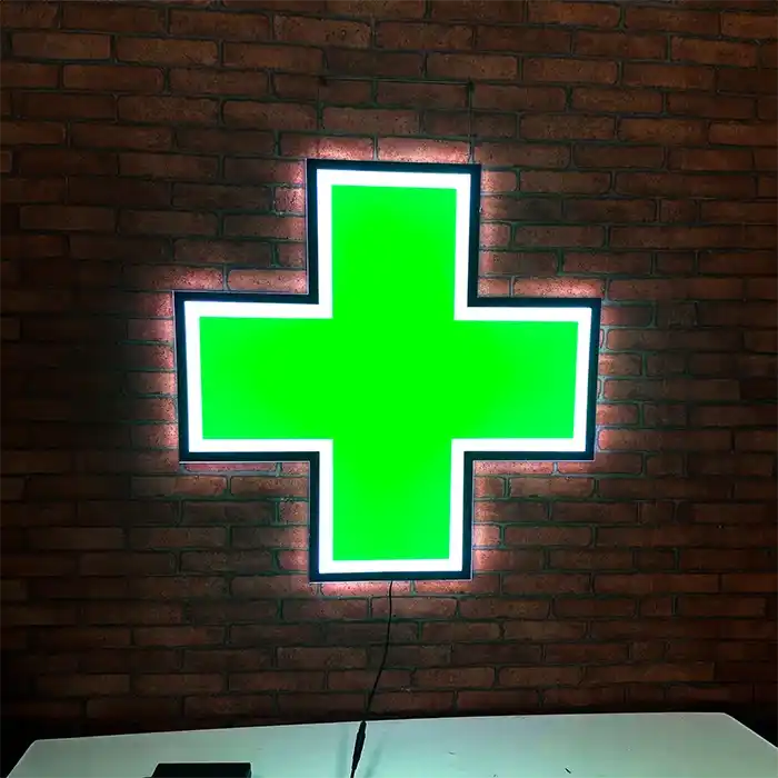 Green cross LED sign lit up against a dark red brick wall inside of a cannabis dispensary