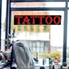 Tattoo LED shop sign above a man giving a tattoo in front of a very large window