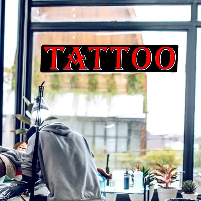 Tattoo LED shop sign above a man giving a tattoo in front of a very large window