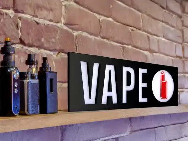 Vape Shop Sign LED sitting on a shelf with vape devices