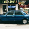 outside view of a (Sisha) Tobacco LED Smoke shop sign with a blue vintage sedan parked infront