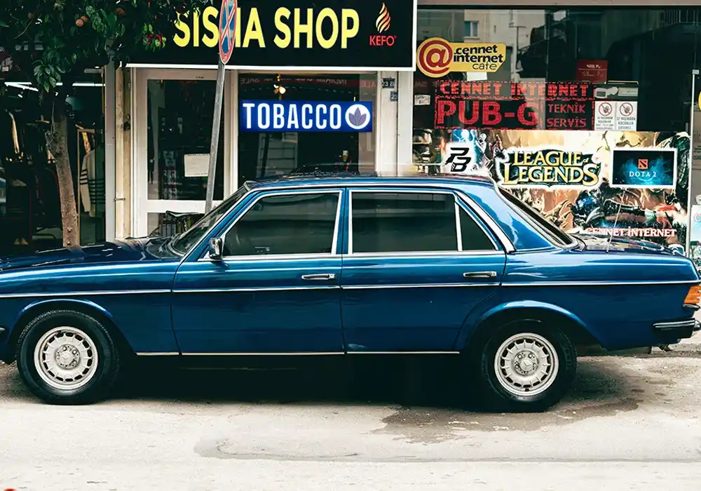 outside view of a (Sisha) Tobacco LED Smoke shop sign with a blue vintage sedan parked infront