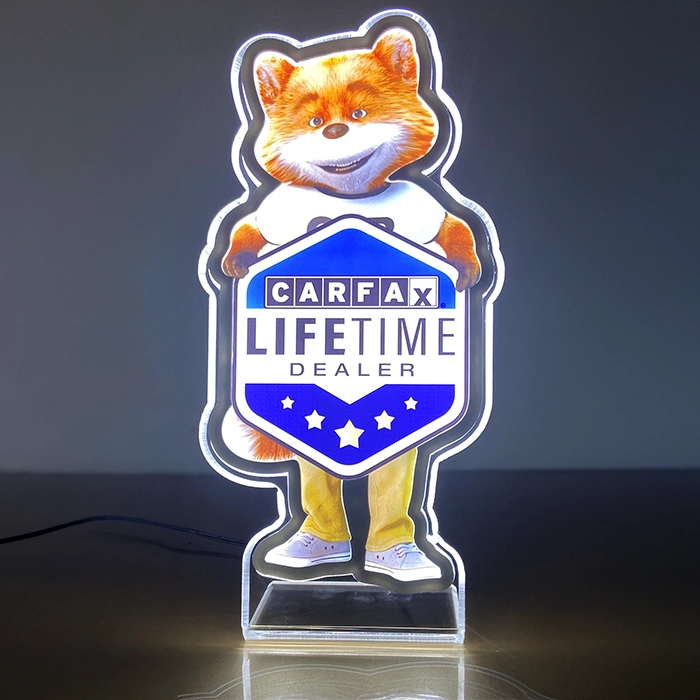 A lighted sign featuring an animated fox character holding a shield-shaped sign that reads "CARFAX Lifetime Dealer." The fox wears yellow pants and a white shirt.
